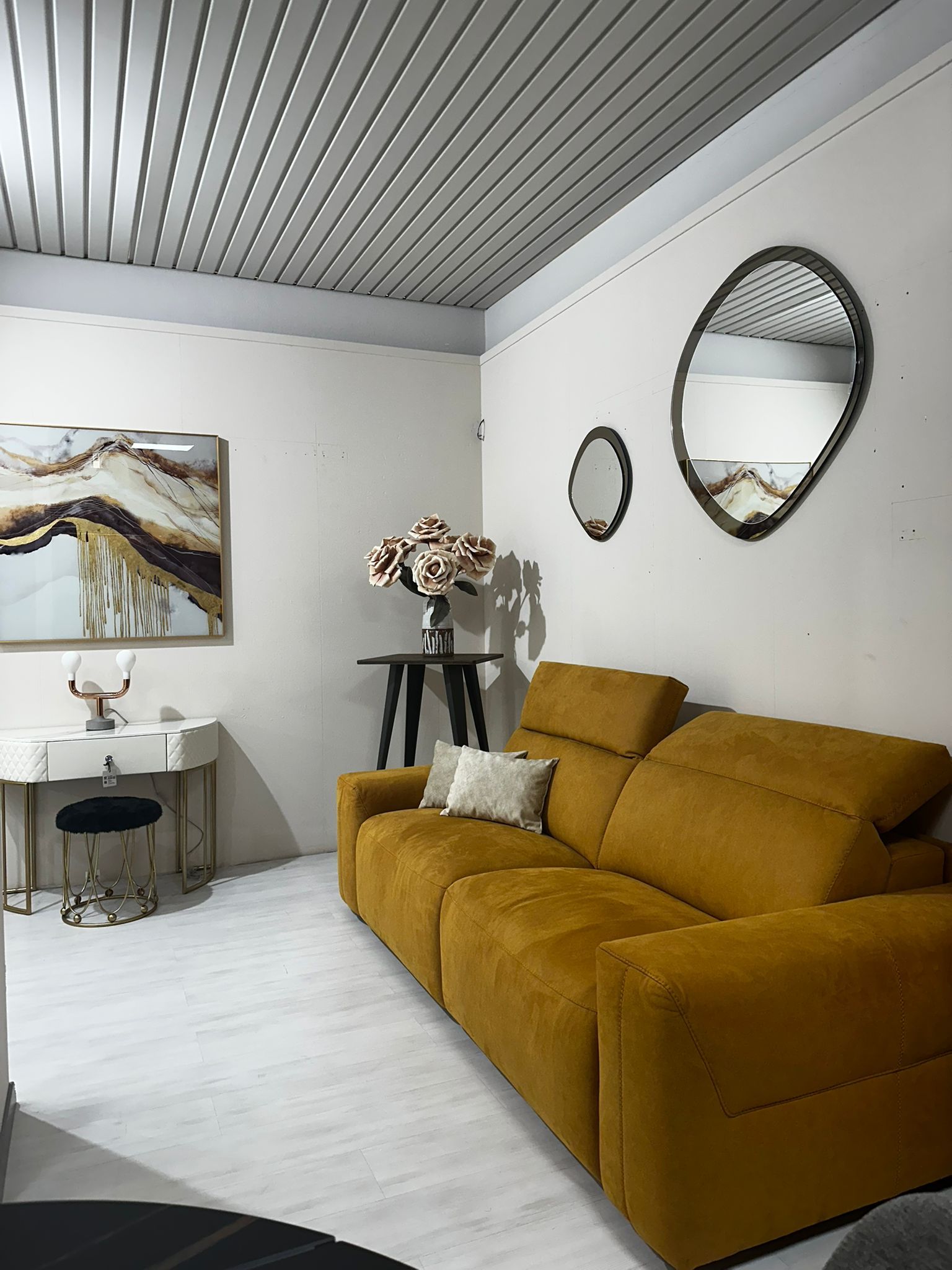 Un soggiorno moderno con un divano color senape, due specchi decorativi e opere d'arte astratta.