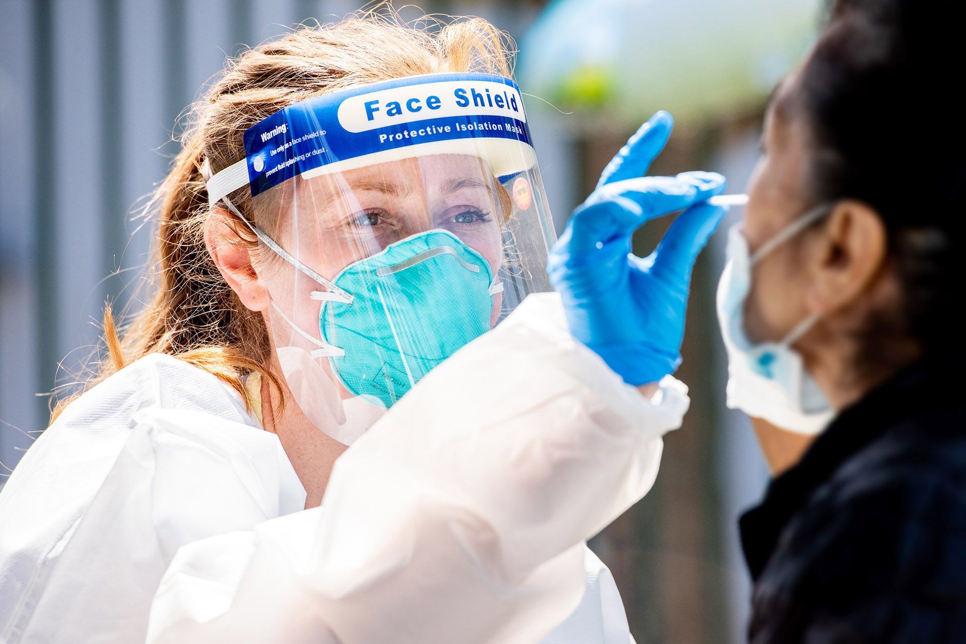 A woman wearing a face shield is taking a swab from another woman.