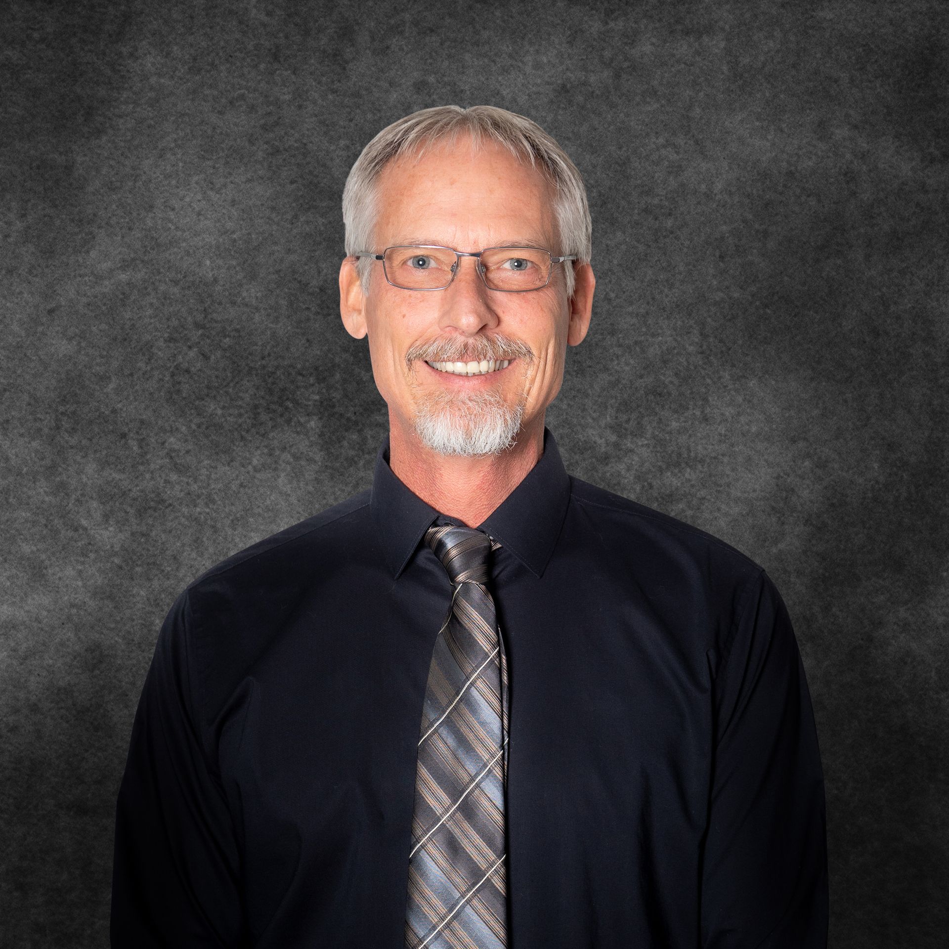 A man wearing a black shirt and tie is smiling for the camera.