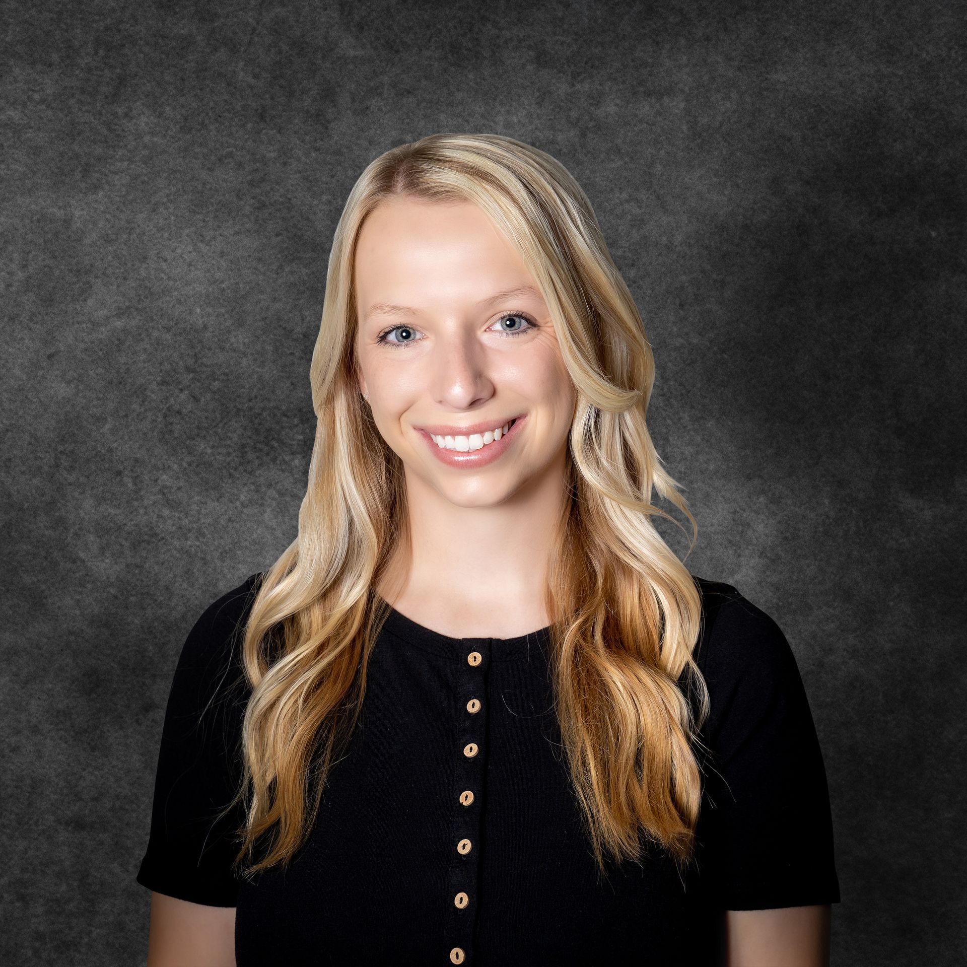 A woman with blonde hair is wearing a black shirt and smiling