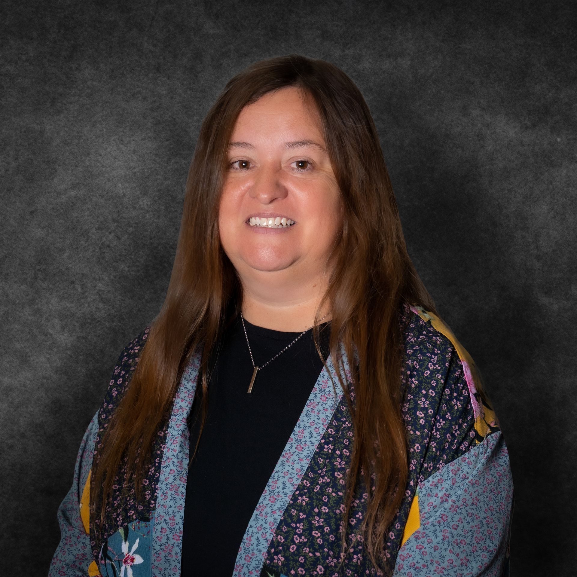 A woman with long hair and a necklace is smiling for the camera.