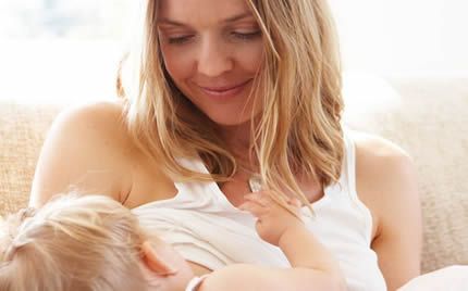 A woman is breastfeeding her baby on a couch.