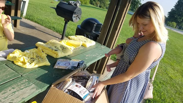 A woman is sitting at a picnic table looking at a box.