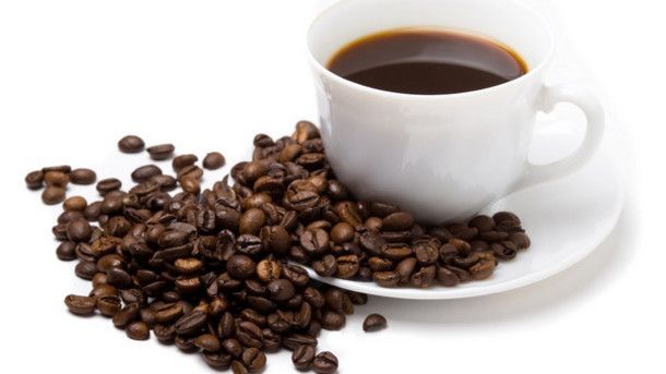 A cup of coffee is on a saucer next to a pile of coffee beans.