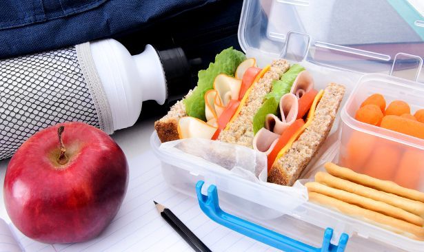 A lunch box filled with a sandwich , apple , crackers , and a water bottle.