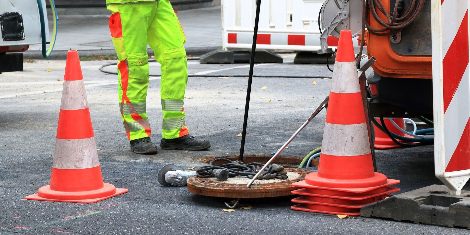 A man is standing next to a manhole cover on the side of the road.