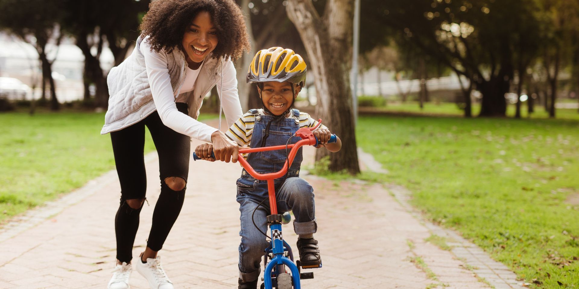 A woman is teaching a young boy how to ride a bike in a park.