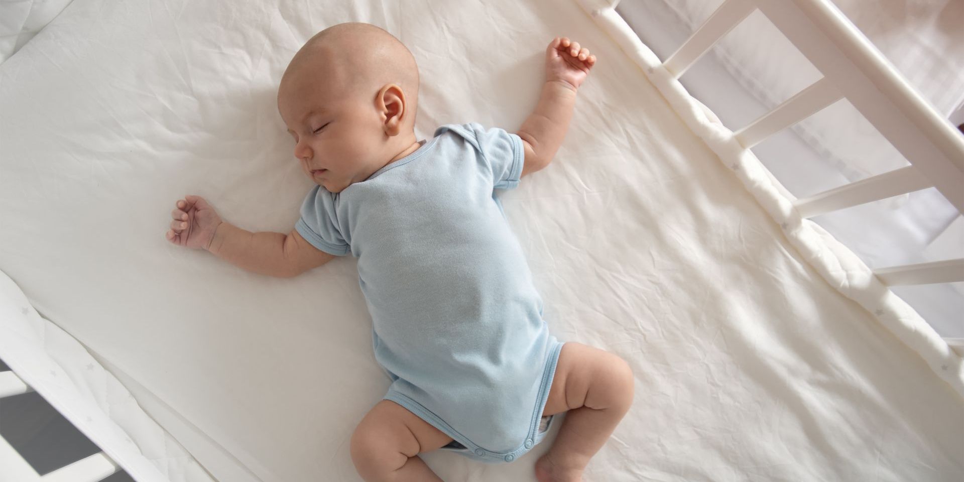 A baby is sleeping in a crib on a white blanket.