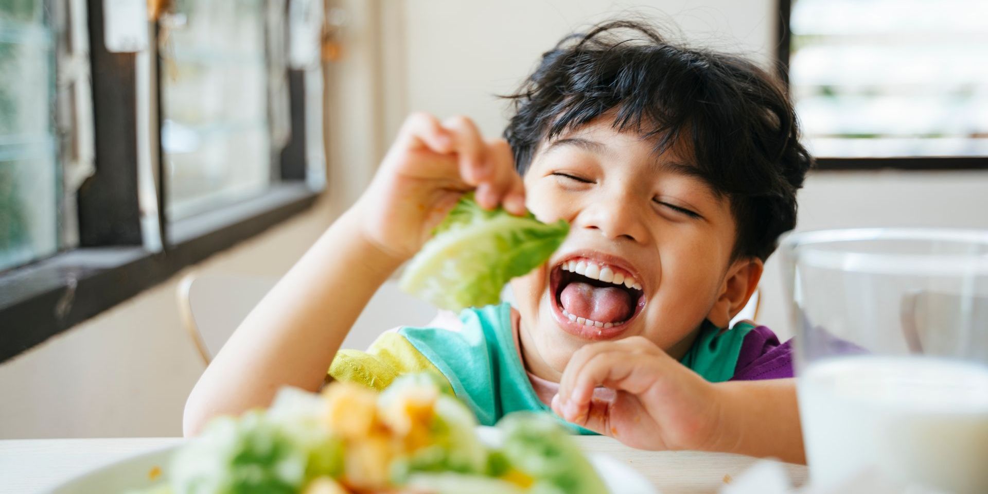 A young boy is sitting at a table eating a salad.