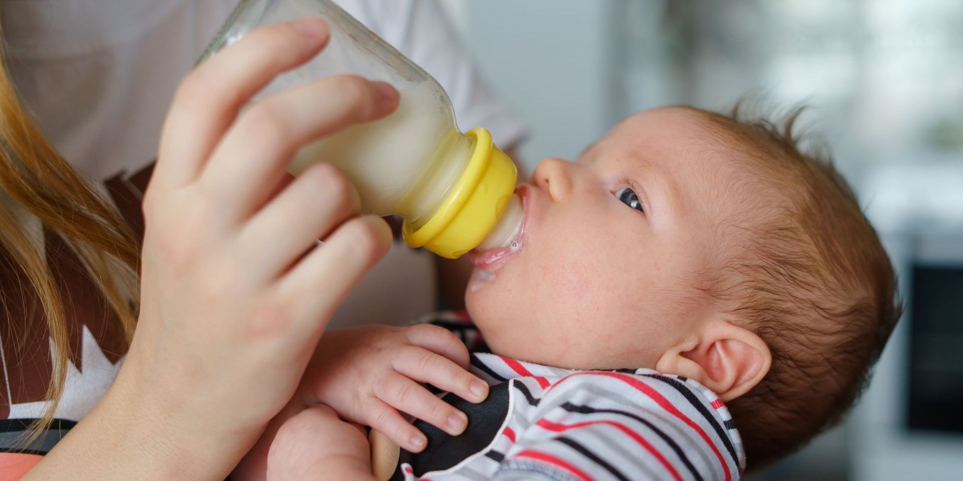 A baby is drinking milk from a bottle while being held by a woman.