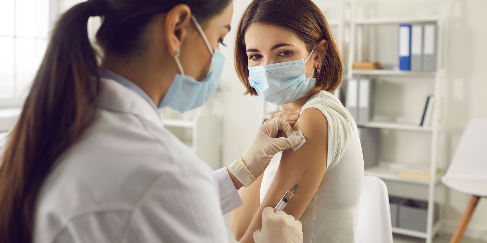 A woman wearing a mask is getting a vaccine from a doctor.