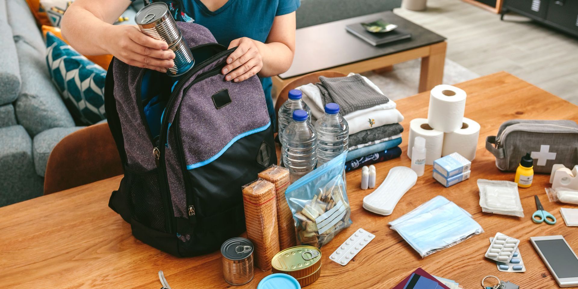 A person is sitting at a table with a backpack filled with emergency supplies.