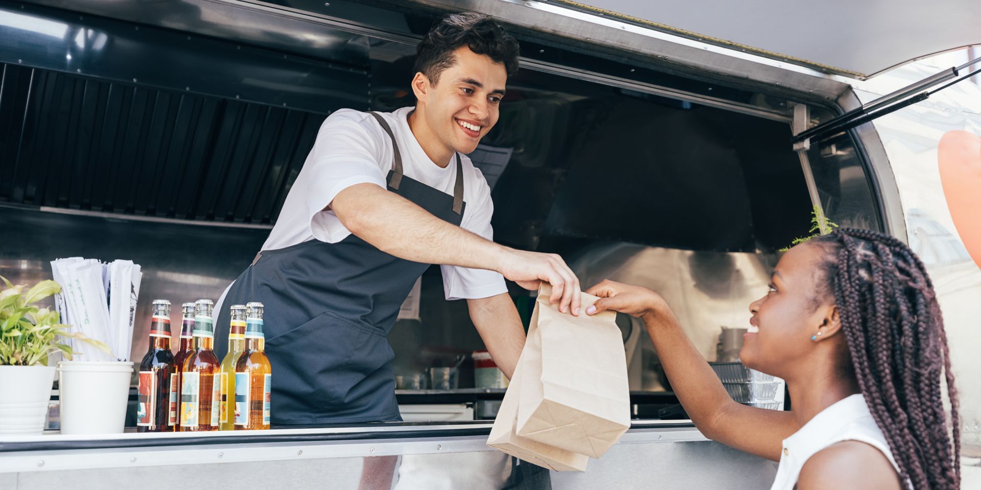 A man is giving a woman a bag of food from a food truck.