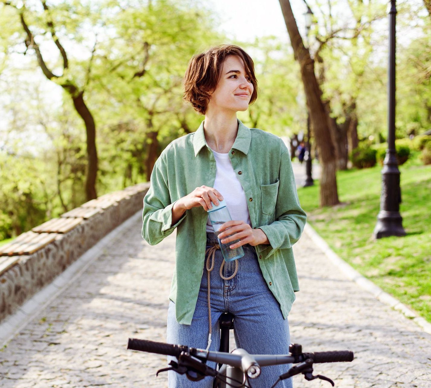 A woman is standing next to a bicycle on a path in a park.