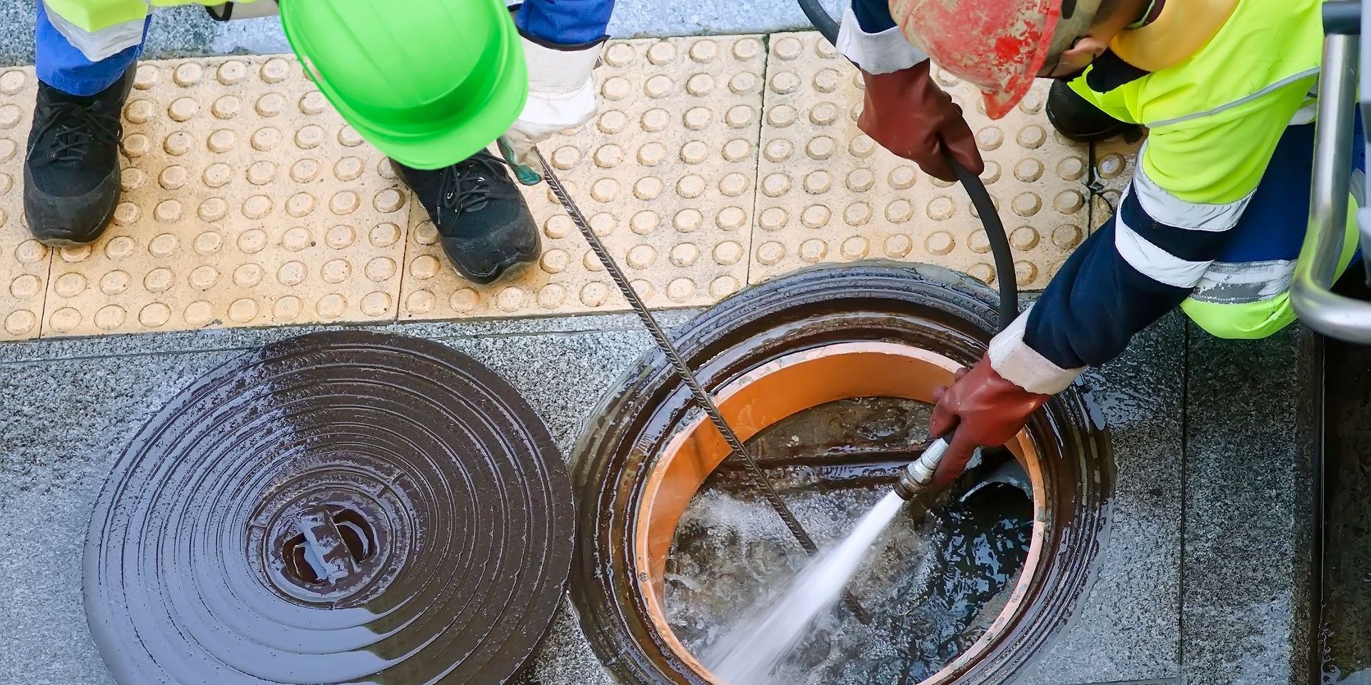 A group of men are cleaning a manhole cover with a high pressure washer.