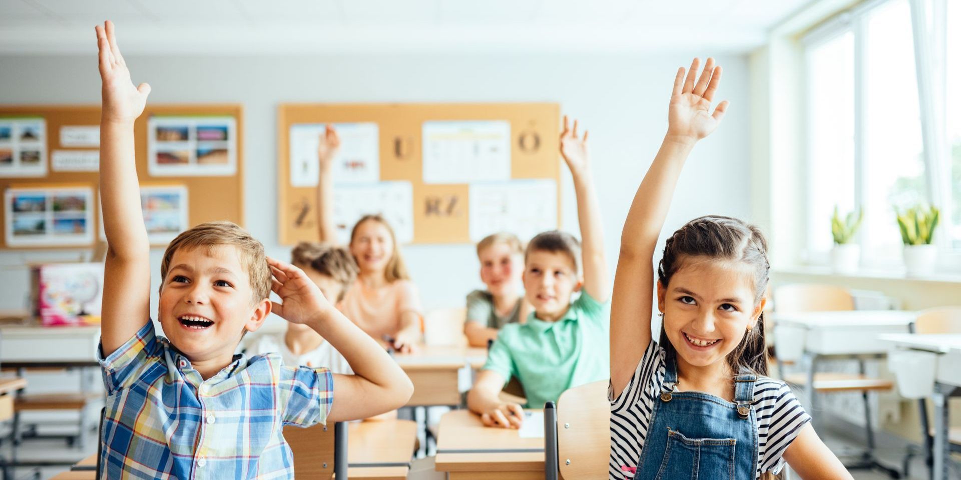 A group of children are raising their hands in a classroom.