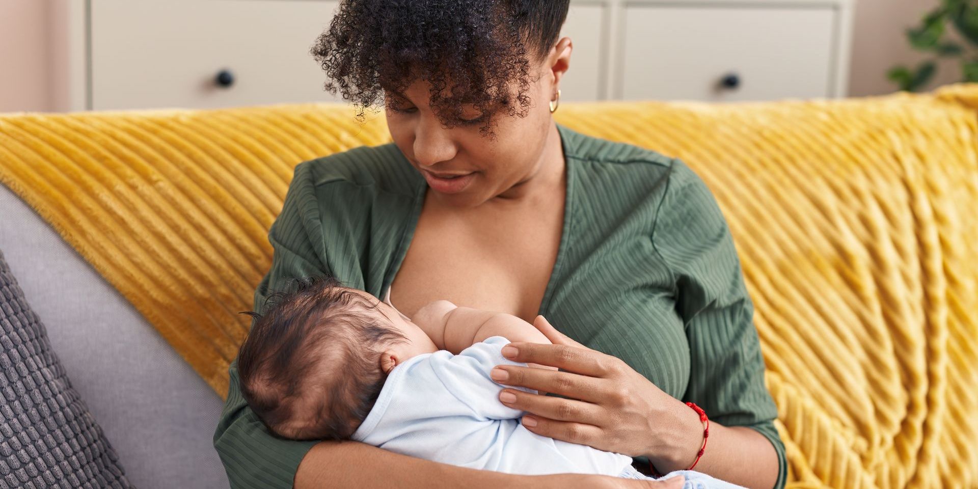 A woman is breastfeeding her baby on a couch.