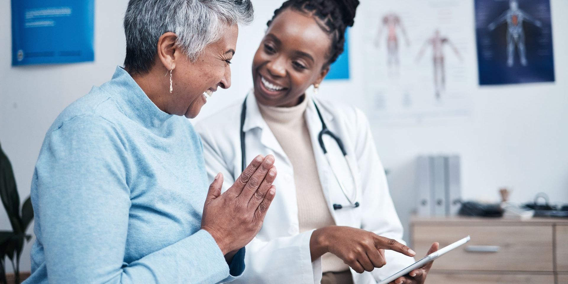 A doctor is talking to an older woman while looking at a tablet.