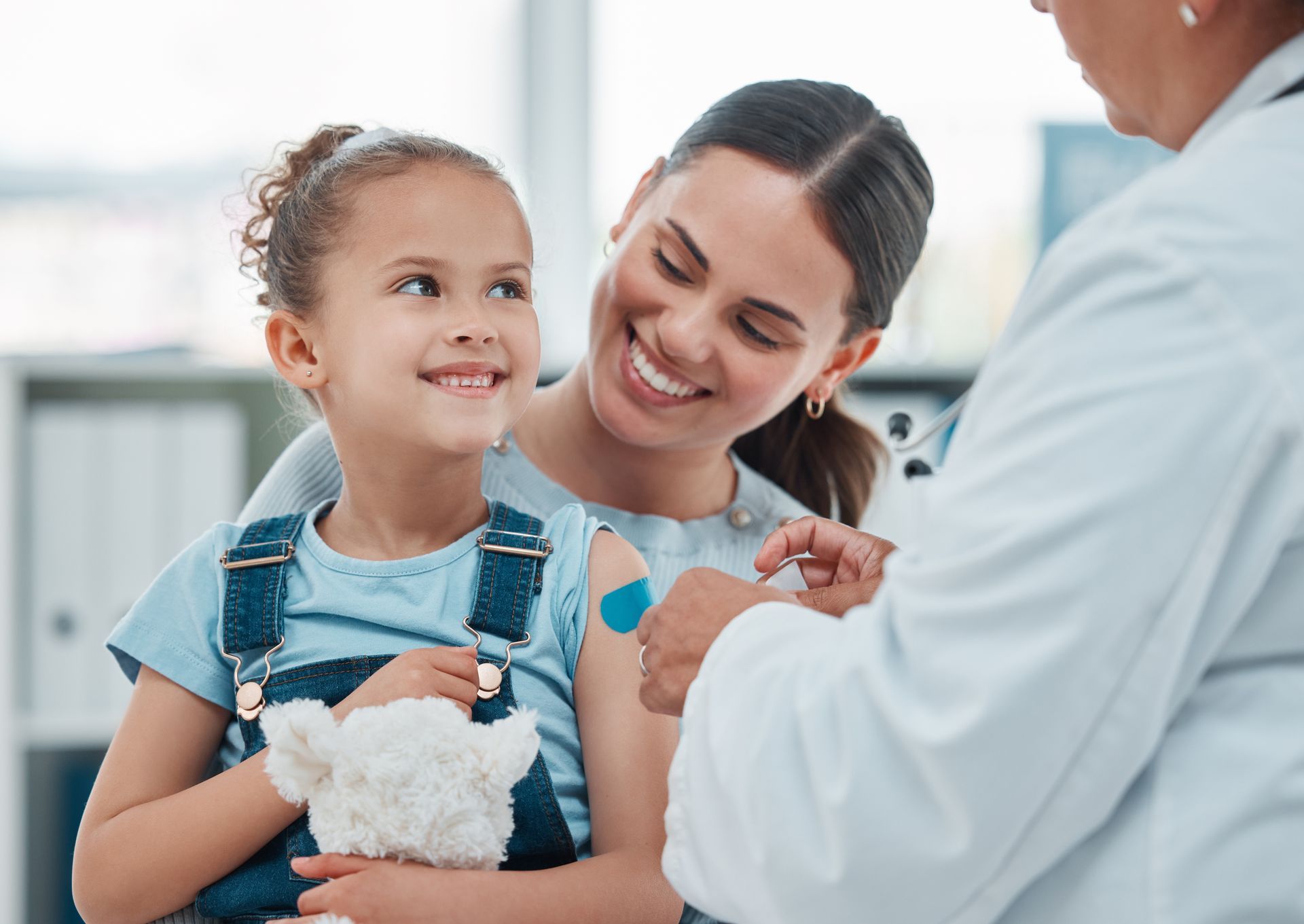 A little girl is getting an injection from a doctor while holding a stuffed animal.