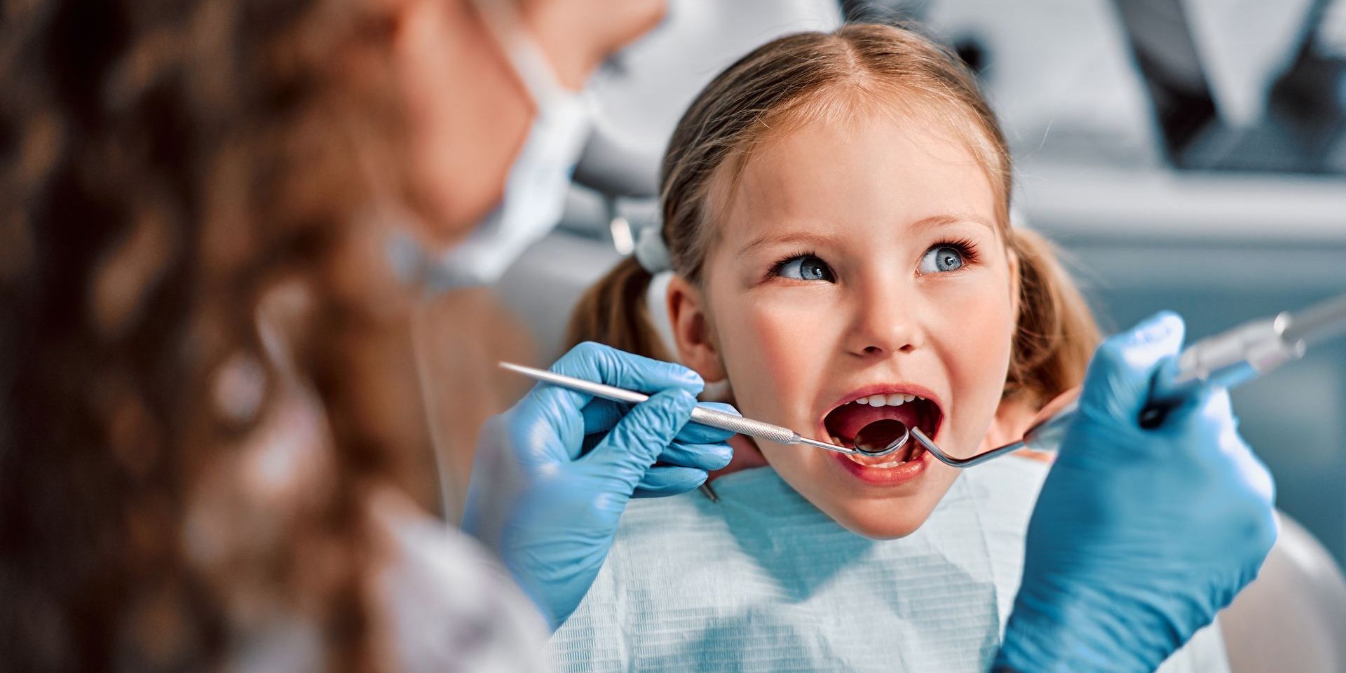 A little girl is getting her teeth examined by a dentist.