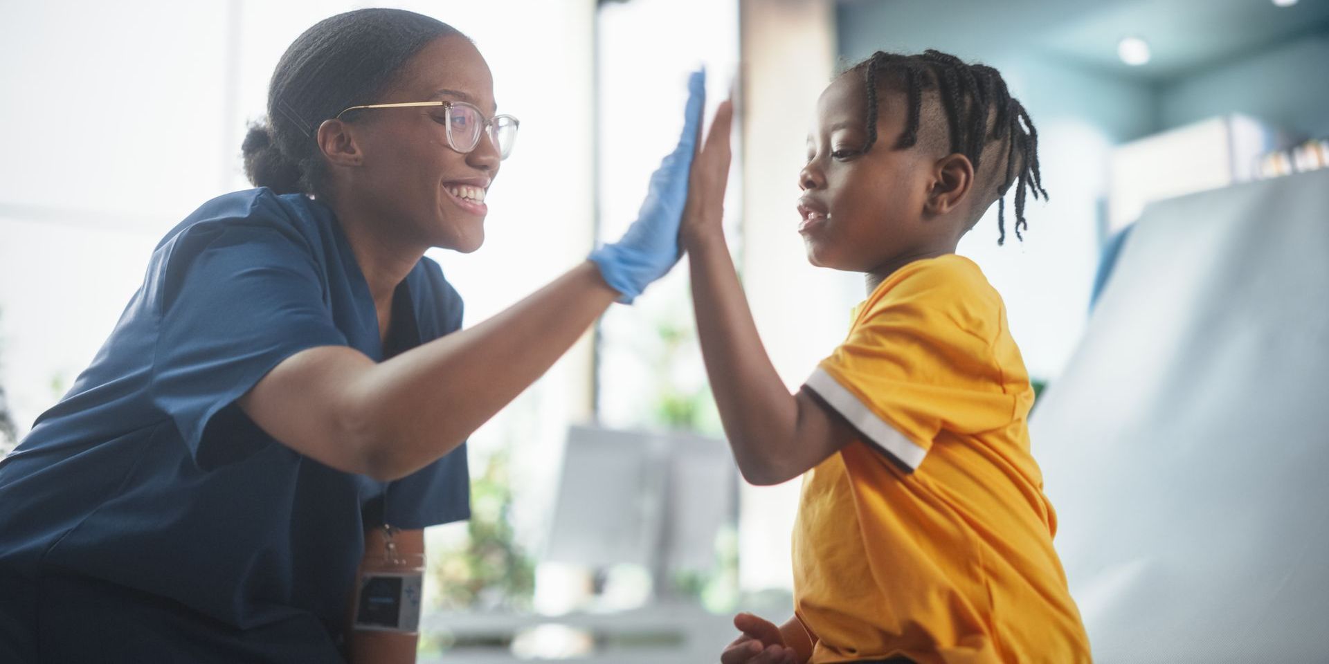 A nurse is giving a child a high five in a hospital room.