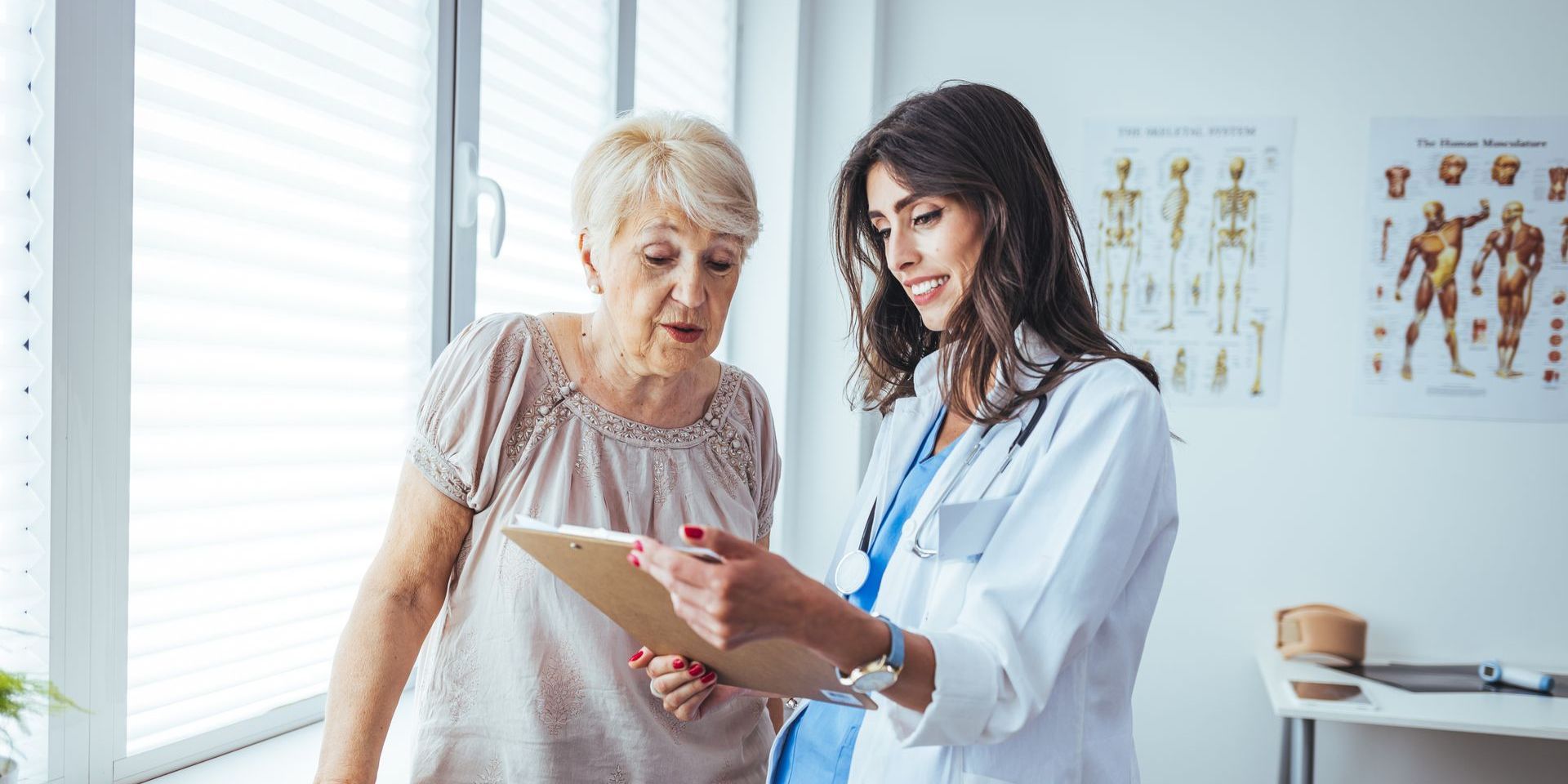 A doctor is talking to an elderly woman while looking at a tablet.