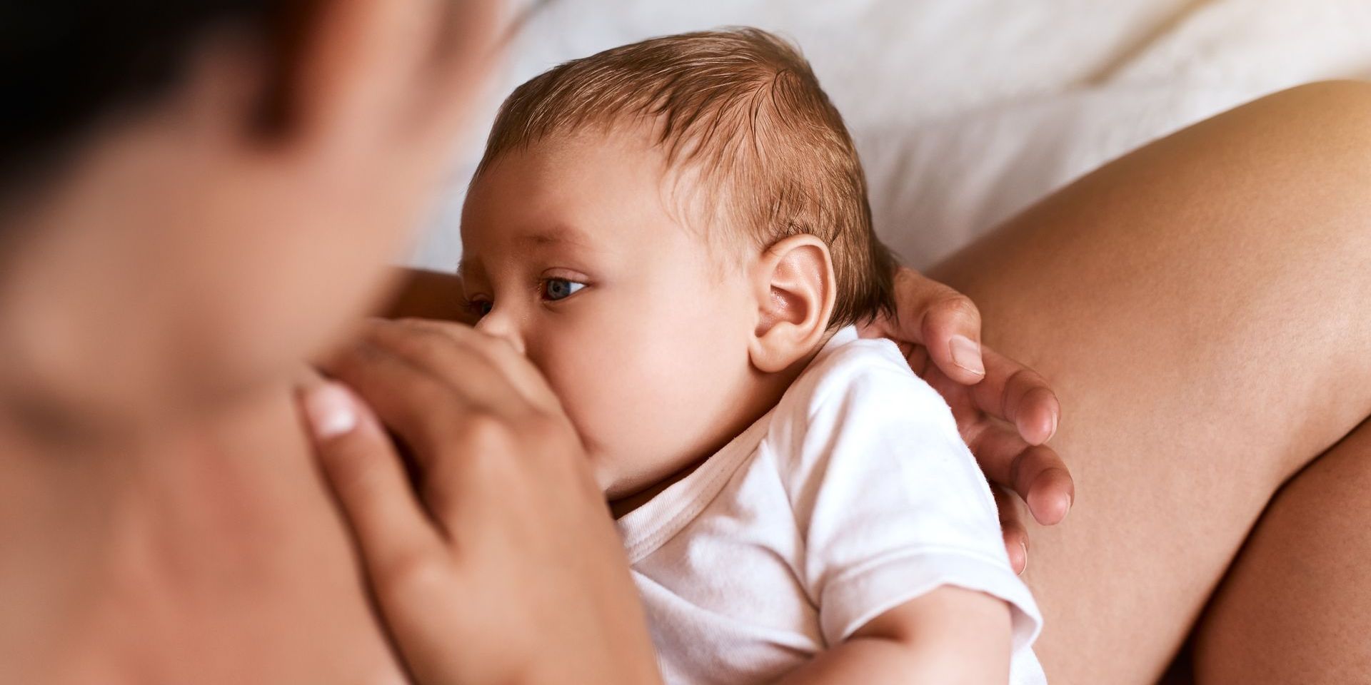 A woman is breastfeeding her baby on a bed.