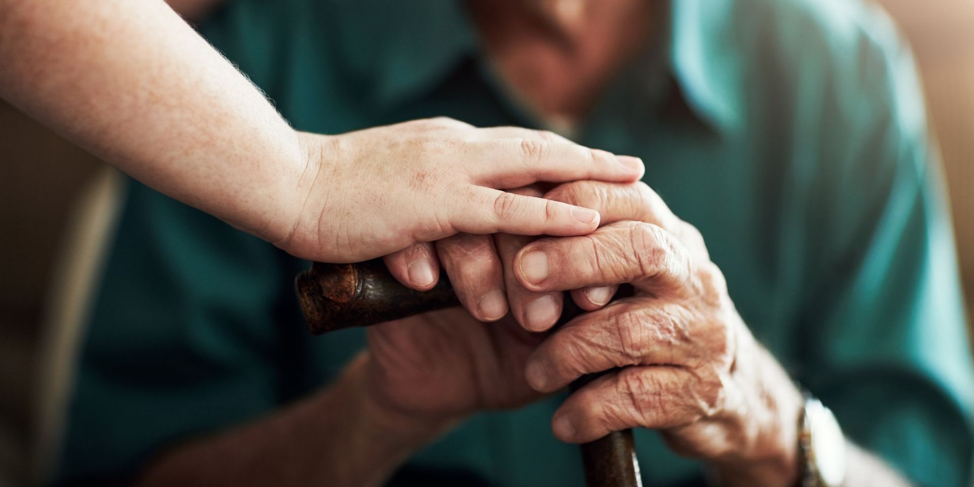 A woman is holding the hand of an elderly man with a cane.