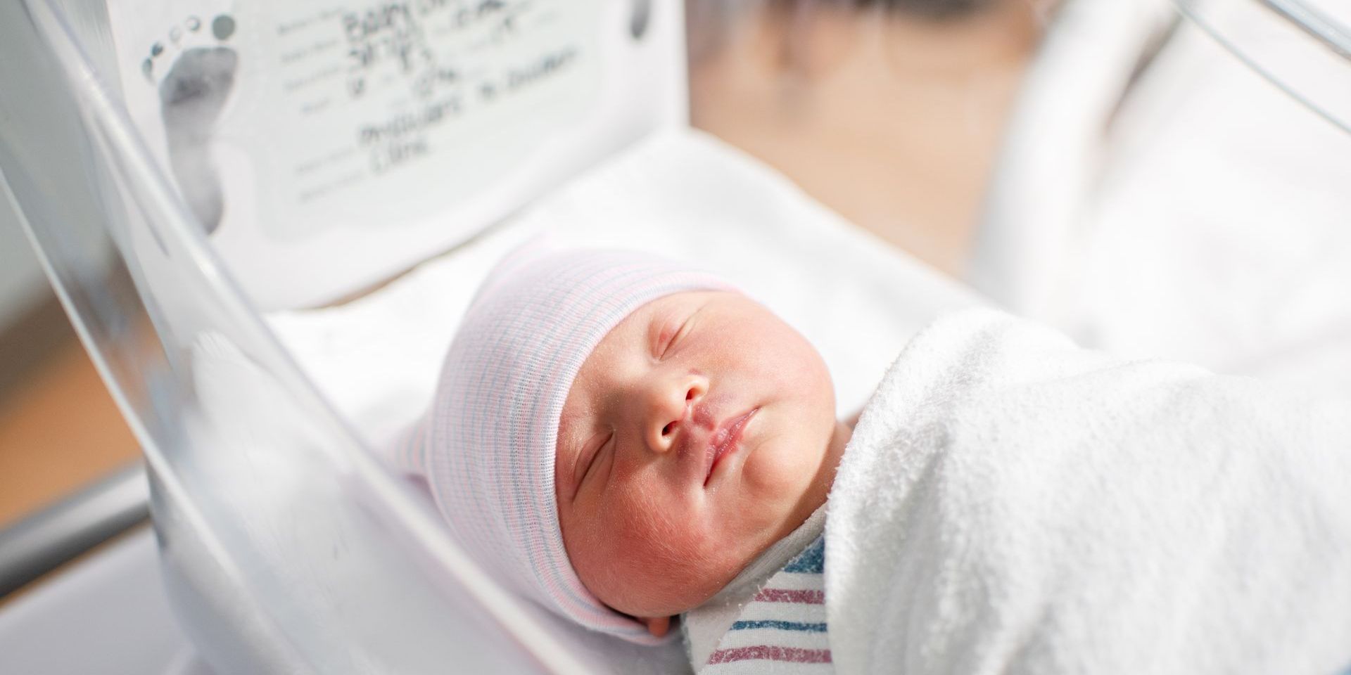 A newborn baby is sleeping in a hospital bed.