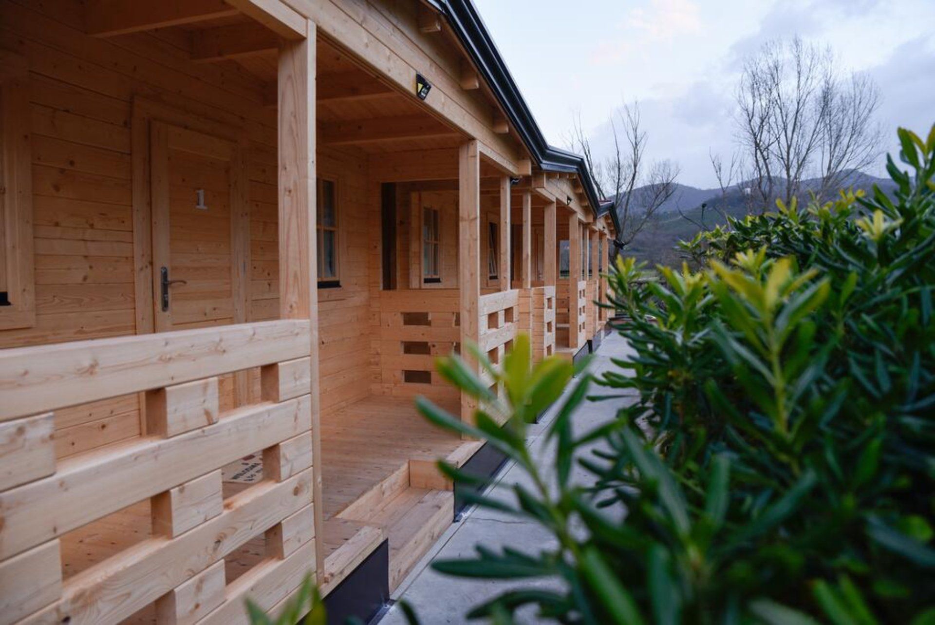 Una casa di legno con portico e scale è circondata da alberi e cespugli.