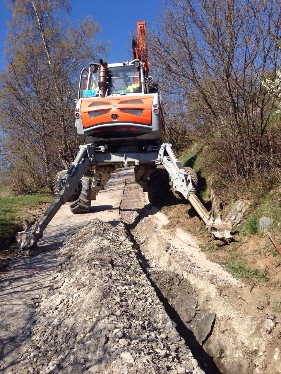 Un véhicule utilitaire tout-terrain orange aux longs pneus roule sur un chemin de terre rocailleux entre des arbres dénudés.