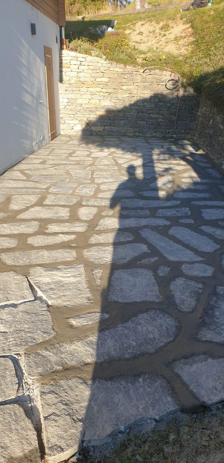 Cour pavée avec un mur d'immeuble à gauche et une ombre au sol sous un soleil éclatant