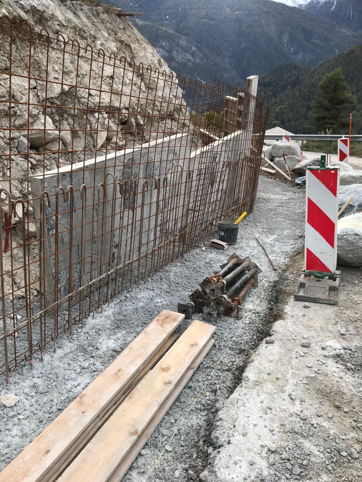 Zone de travaux en bord de route avec barrière de sécurité en fer à béton, bois de construction et poteaux de signalisation rouge et blanc au bord d'une route de montagne