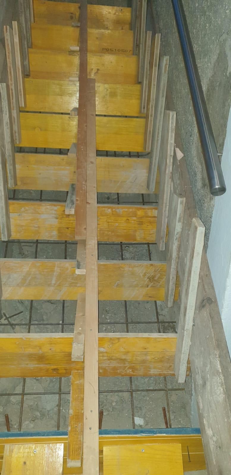 Escalier étroit en béton avec marches jaunes et rampes métalliques, vu du dessus
