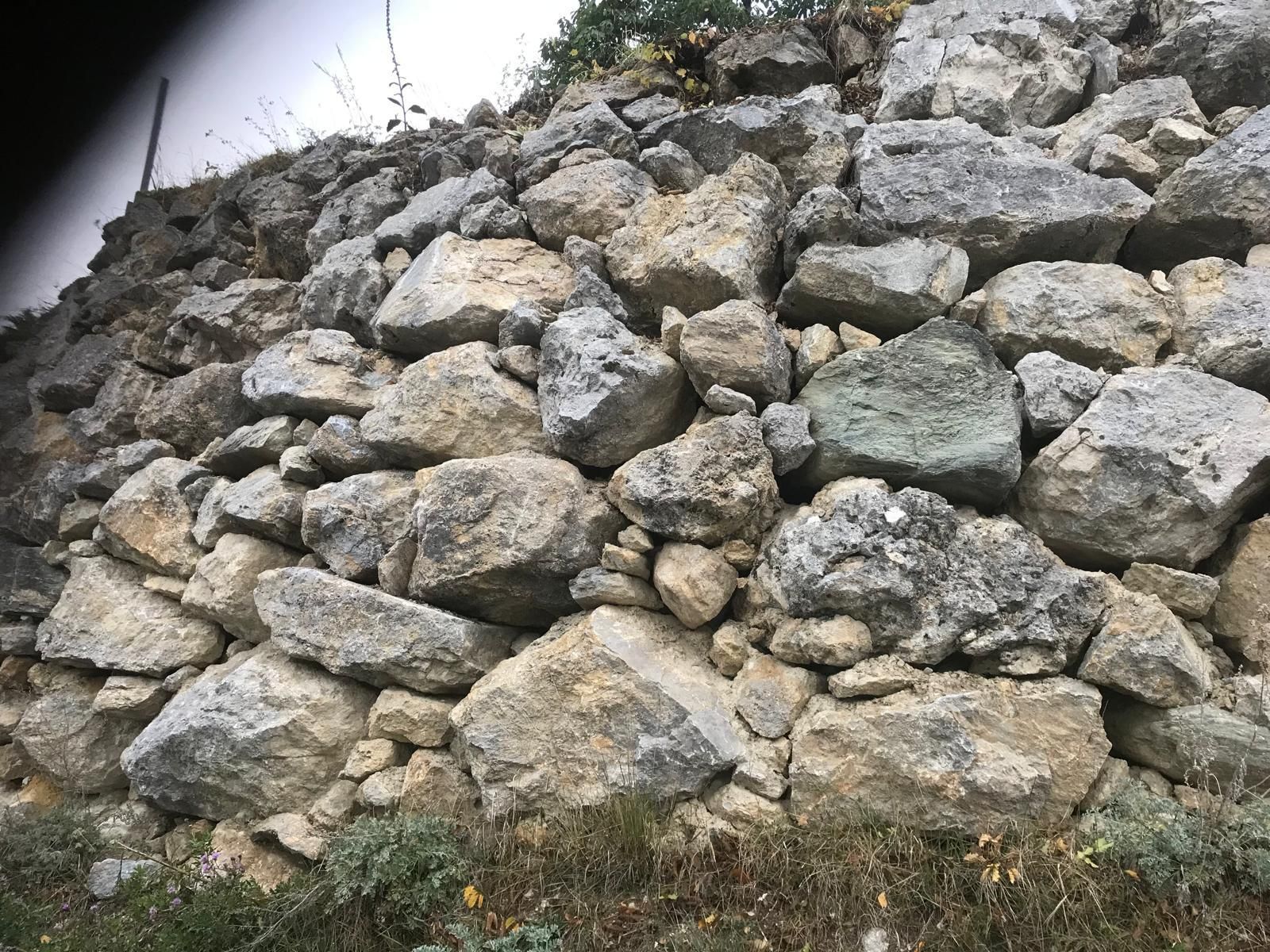 Des roches grises empilées forment un talus de pierres grossières à côté d'une herbe clairsemée et de terre.