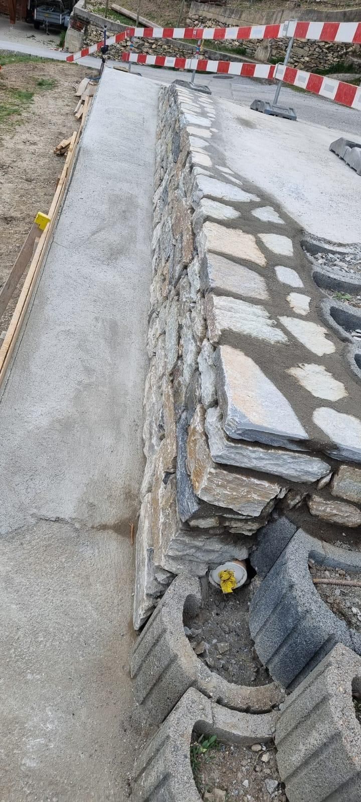 Trottoir endommagé à côté d'un mur de pierre et de barrières rouges et blanches sur une zone de travaux routiers