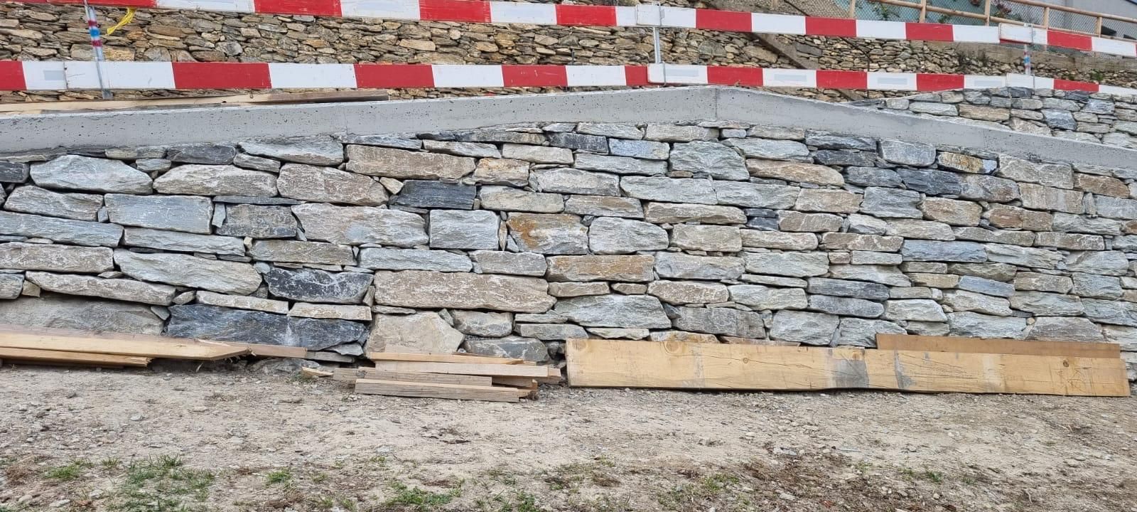 Mur de soutènement en pierre avec une barrière à rayures rouges et blanches en partie supérieure et une planche de bois à la base.