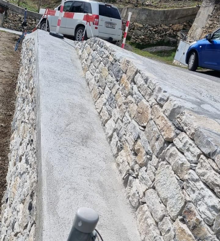 Rampe en pierre abrupte au bord d'une route, avec une camionnette blanche et une voiture bleue garées à proximité.