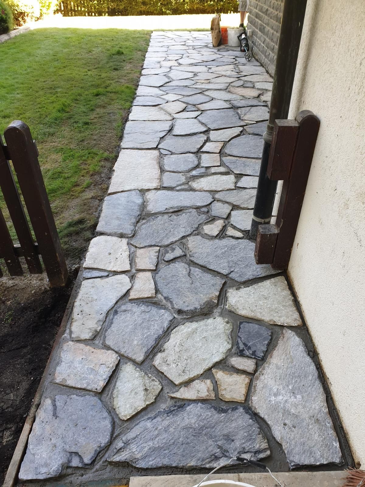 Allée en pierre longeant une pelouse, bordée d'un mur et de piliers de portail.