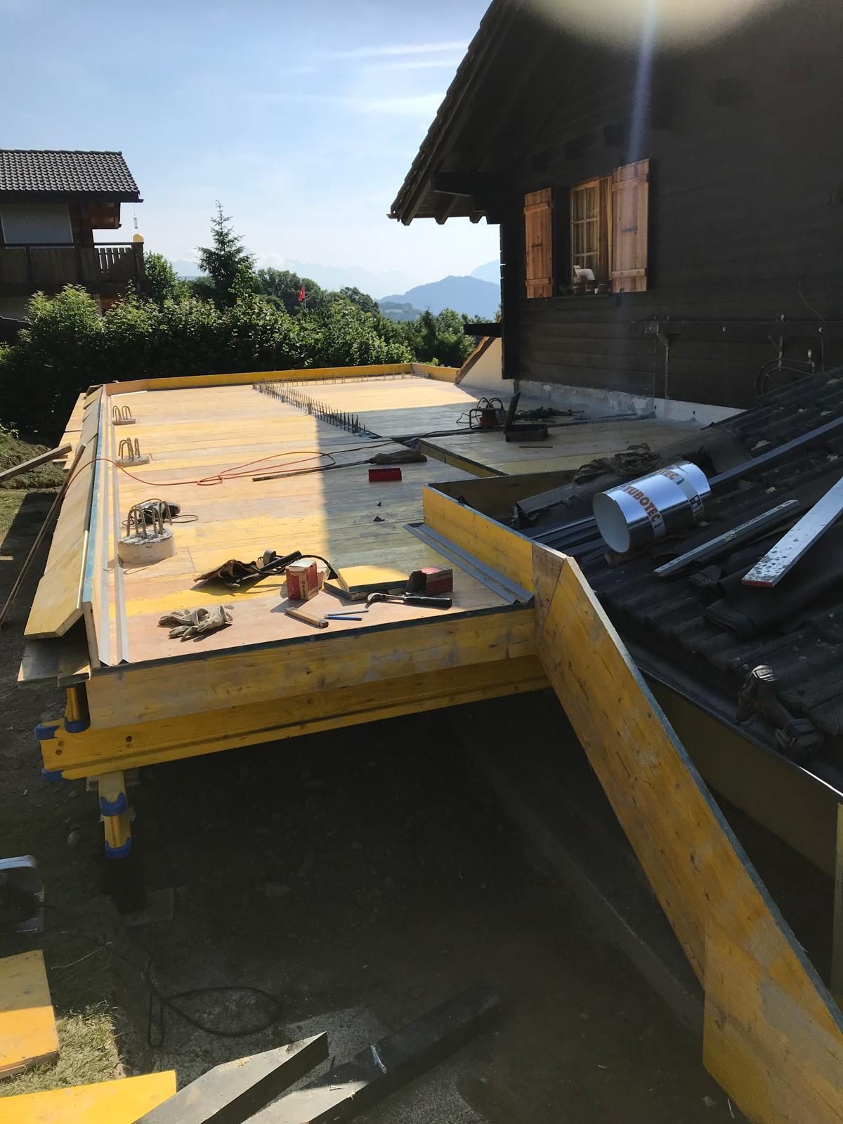Toiture endommagée avec une grande section recouverte de contreplaqué et des matériaux épars à côté d'une maison.