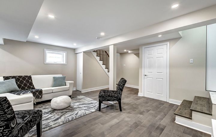 A living room in a basement with a couch , chairs , and stairs.