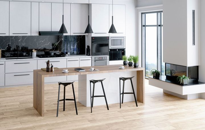 A kitchen with white cabinets , wooden floors , stools and a fireplace.