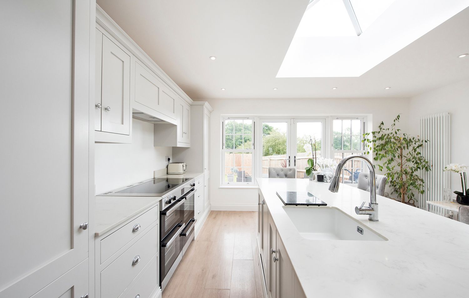 A kitchen with white cabinets , a sink , a stove , and a skylight.