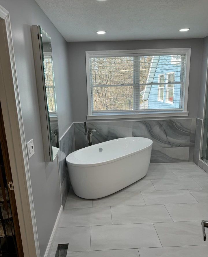 A bathroom with a tub , mirror , and window.