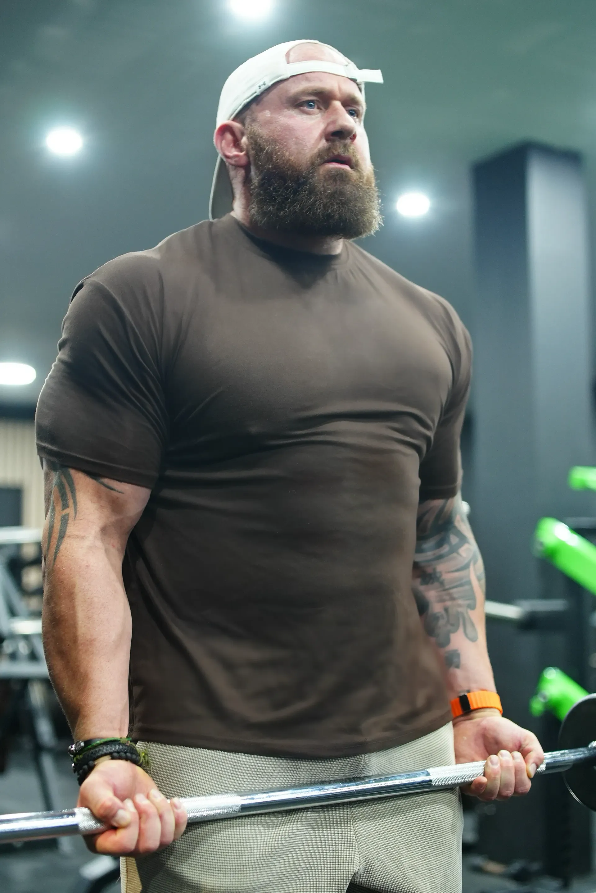 A man with a beard is lifting a barbell in a gym.