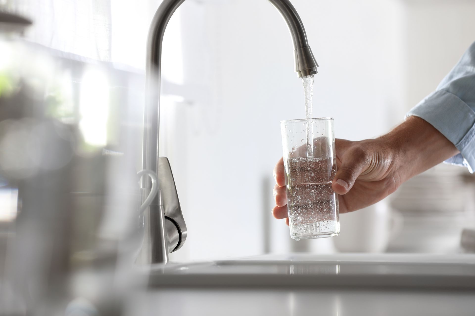 A person is pouring water into a glass from a faucet.
