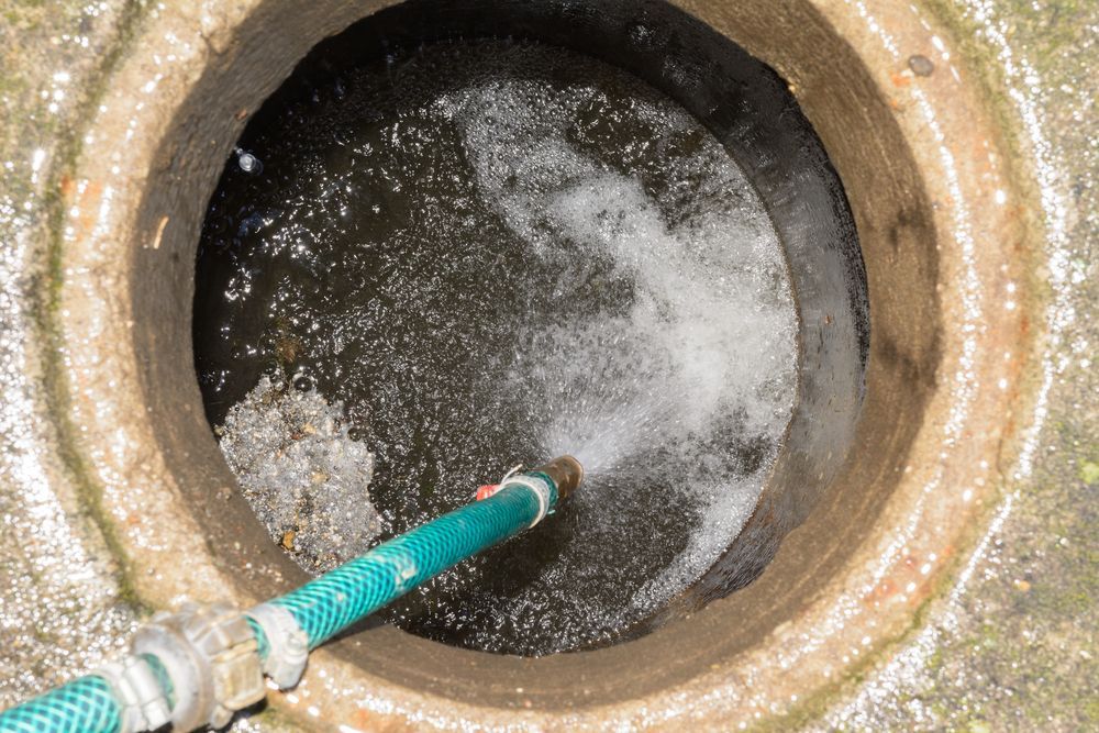 A green hose is being used to clean a drain.