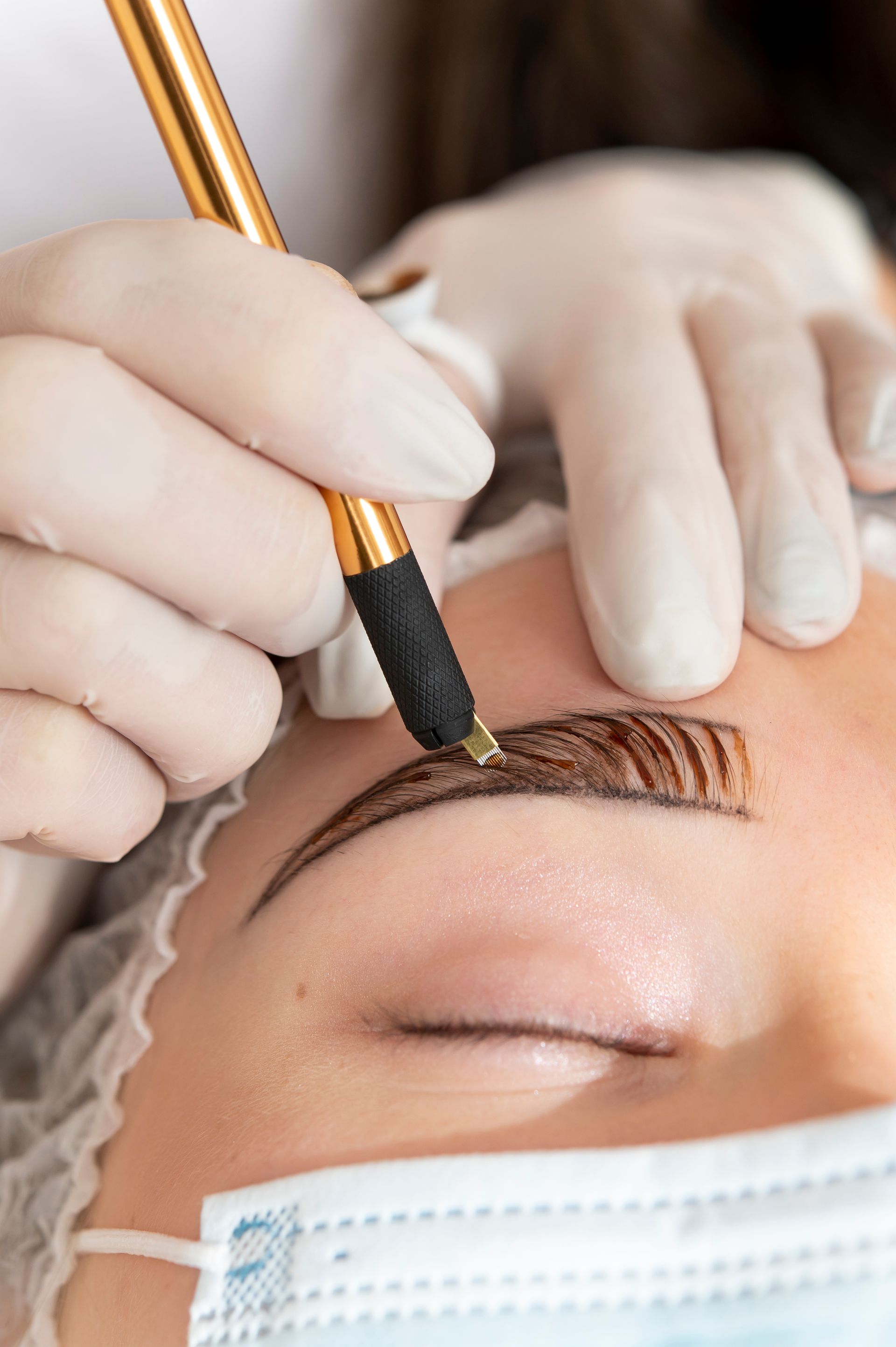 A woman is getting her eyebrows tattooed with a pen.