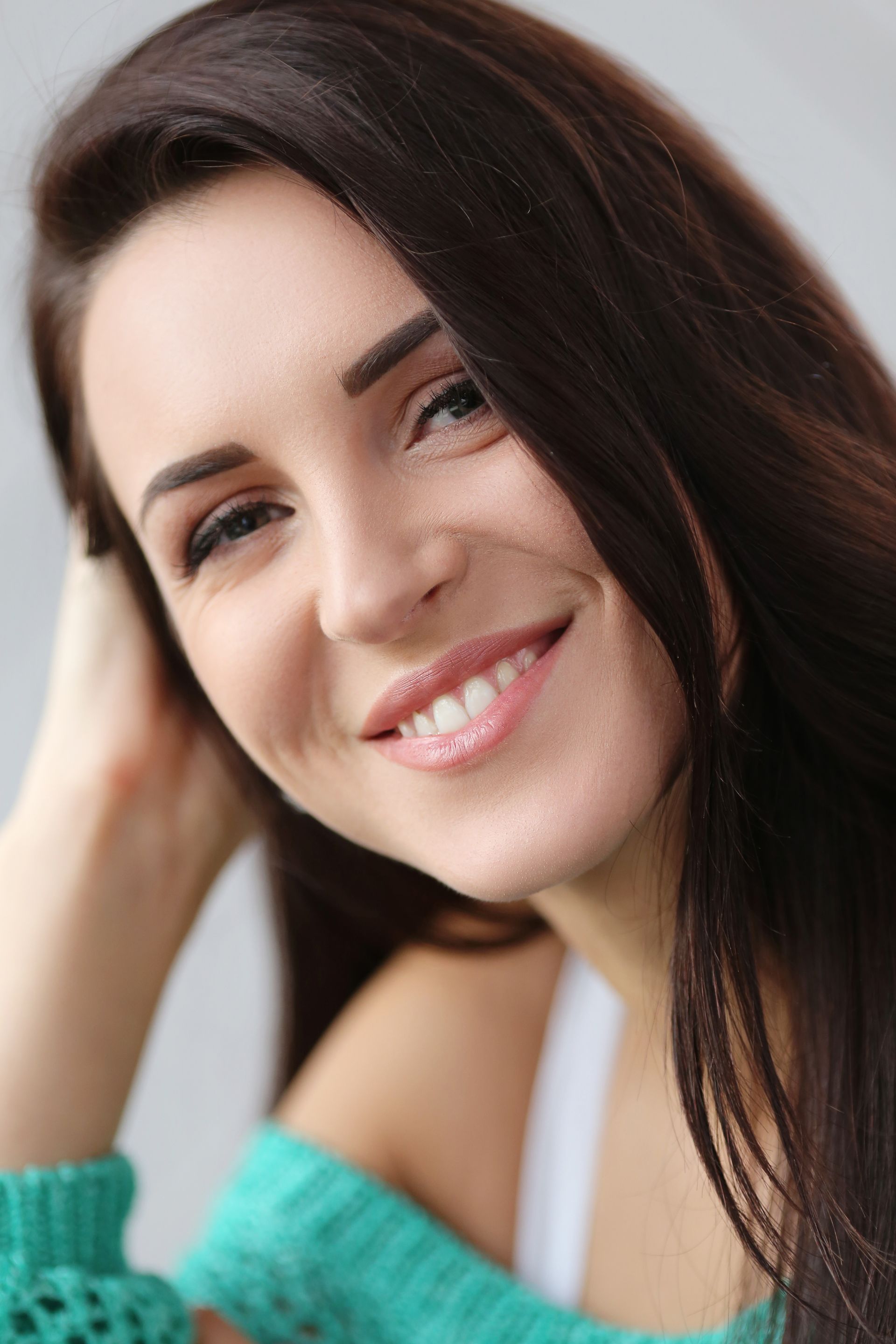 A woman in a green sweater is smiling and touching her hair.