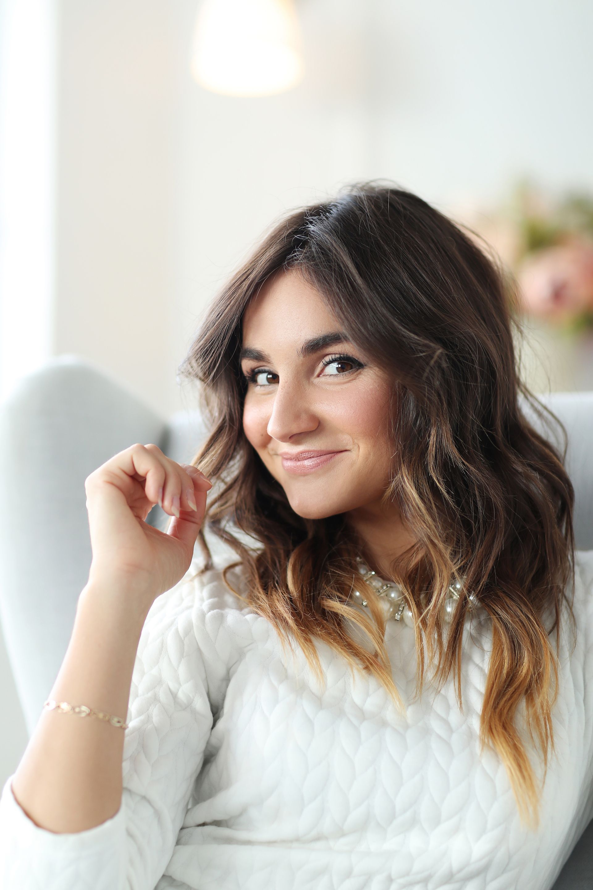 A woman in a white sweater is sitting on a couch and smiling.